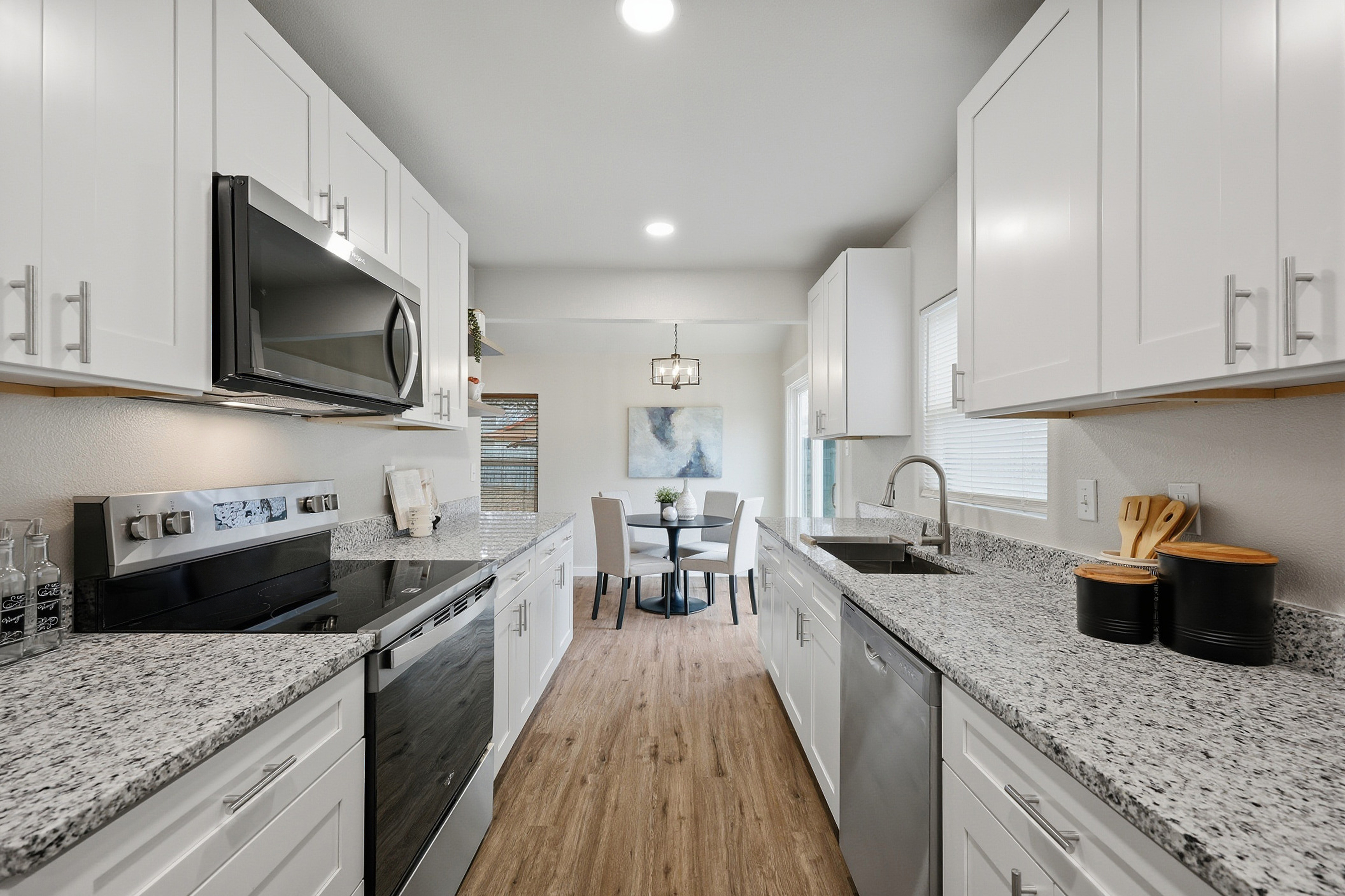 Full galley kitchen view showing white cabinetry run, granite countertops, and stainless appliances